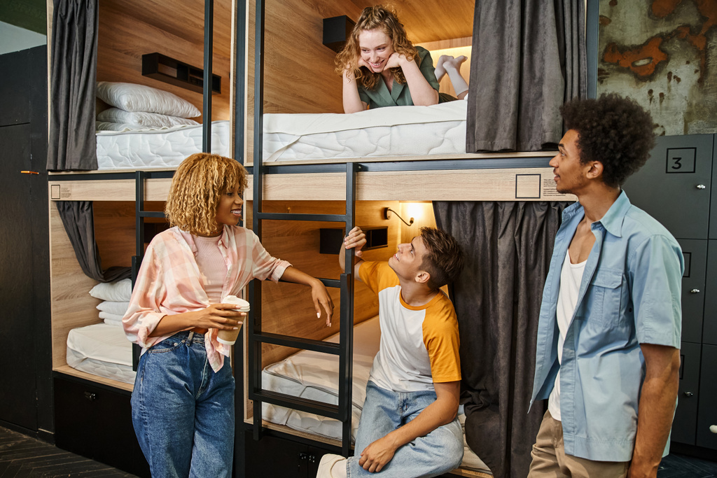 radosnych wieloetnicznych przyjaciół patrząc na młodą kobietę leżącą na dwupiętrowym łóżku w hostelu studenckim - Zdjęcie, obraz