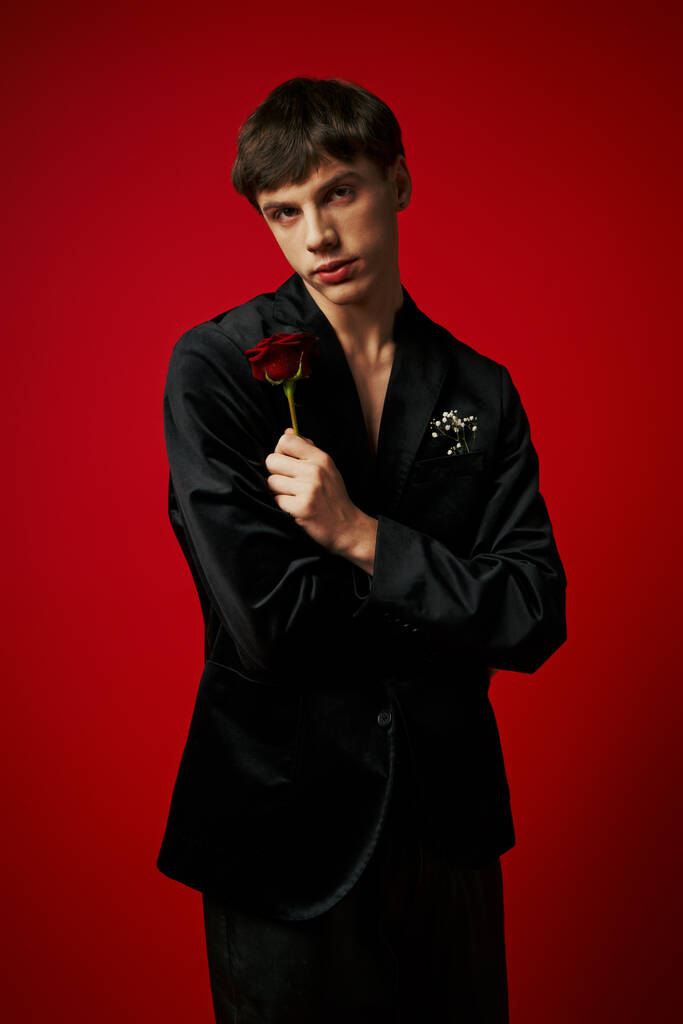 portrait de mec romantique tenant rose dans la main et regardant la caméra sur fond rouge, fleur - Photo, image