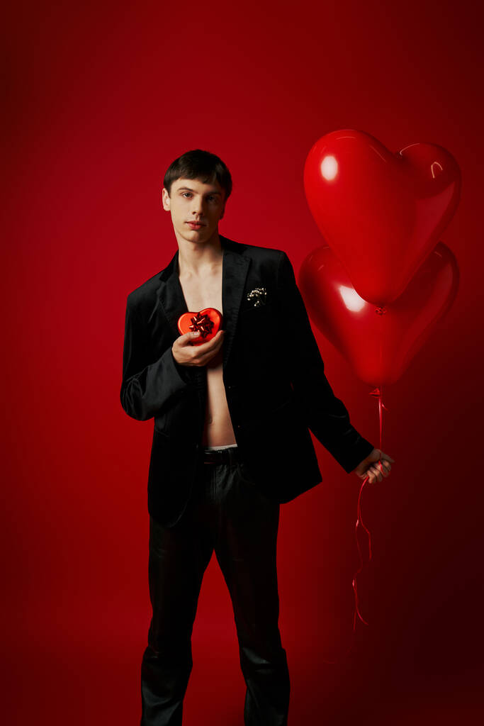 romantikus fiatalember gazdaság szív alakú ajándék doboz és lufik piros alapon, Valentin nap - Fotó, kép