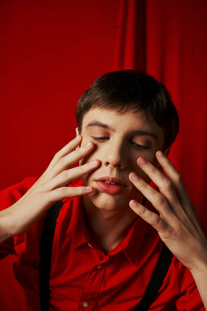 close up photo, pensive young man in shirt and suspenders touching his face on red background - Photo, Image