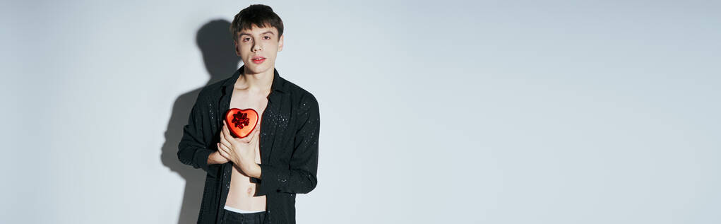 Kırmızı kalp şeklinde tişörtlü yakışıklı bir adam gri arka planda hediye kutusu, Sevgililer Günü afişi - Fotoğraf, Görsel