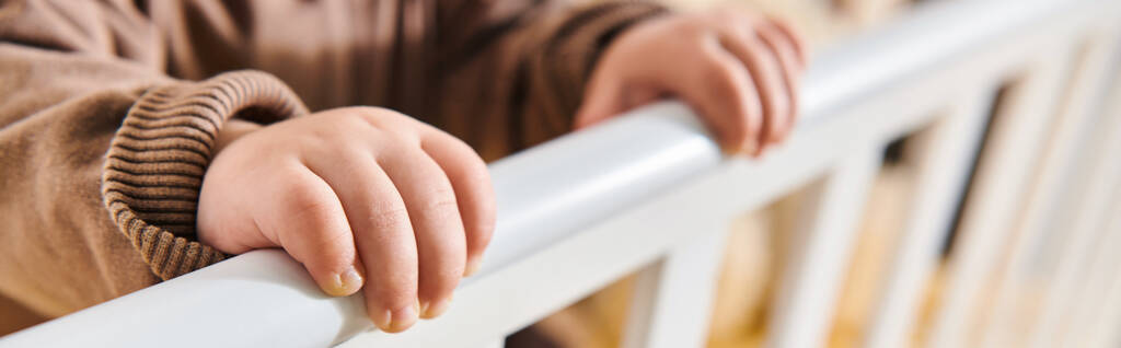 enfance, petites mains de petit enfant debout dans la crèche dans la chambre d'enfant à la maison, bannière horizontale - Photo, image
