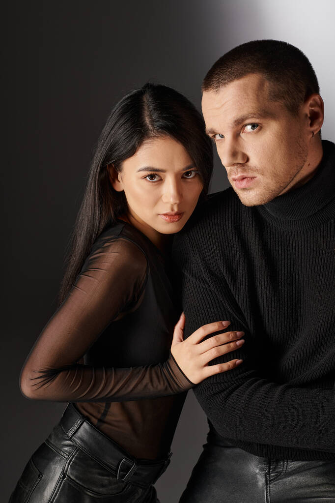 appealing asian woman hugging handsome man in black clothes sitting on grey backdrop with light - Photo, Image