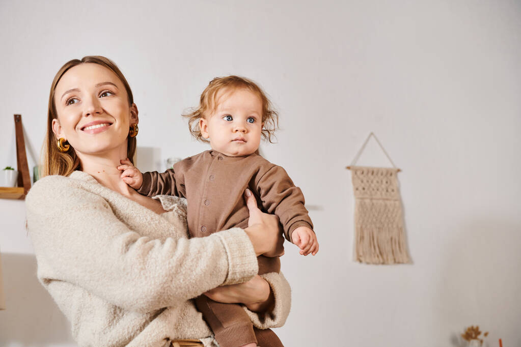 iloinen hymyilevä nainen tilalla ja syleilee poikavauva viihtyisässä lastenhuoneessa, autuas äitiys - Valokuva, kuva