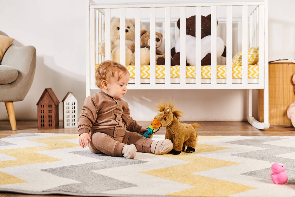 床に座って保育室のベビーベッドの近くでおもちゃの馬で遊ぶ愛らしい幼児の少年 - 写真・画像