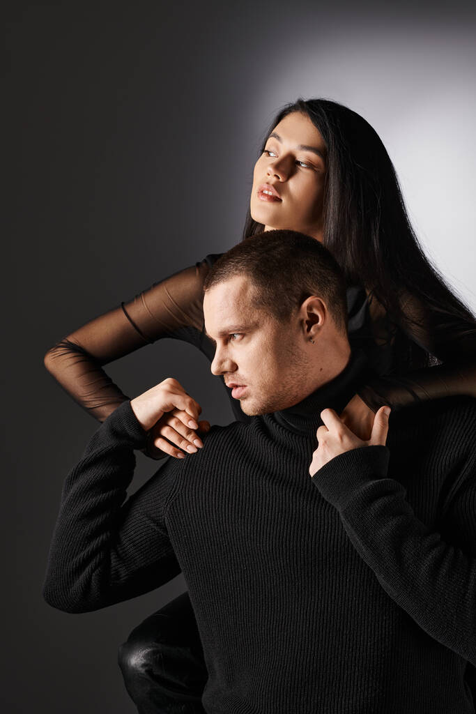 fashionable interracial couple in black clothes holding hands and looking away on grey backdrop - Photo, Image