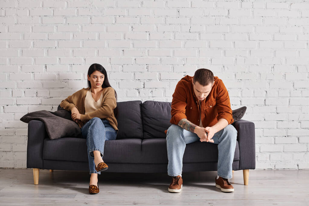 joven frustrado interracial pareja sentado en sofá en sala de estar, familia divorcio concepto - Foto, imagen