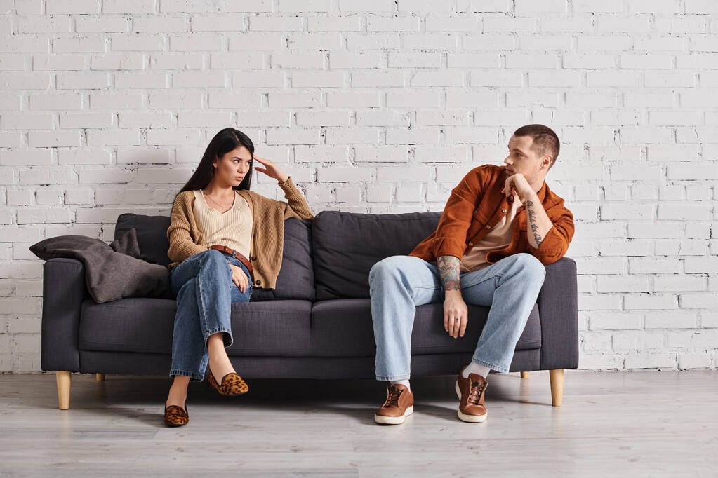 pareja interracial ofendido mirándose el uno al otro en el sofá en la sala de estar, dificultades de relación - Foto, Imagen