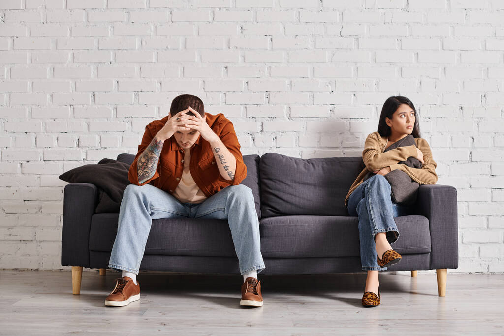 молода депресивна багатоетнічна пара сидить на дивані в сучасній вітальні, концепція сімейного розлучення - Фото, зображення