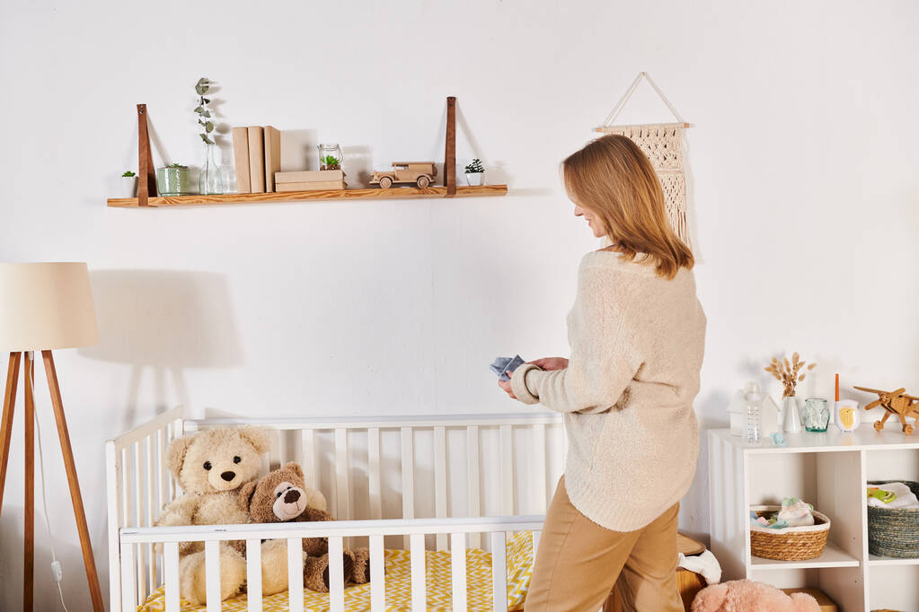 jovem grávida de pé perto berço com brinquedos macios em quarto de crianças em casa, nova expectativa de vida - Foto, Imagem