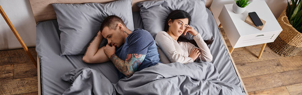 vysoký úhel pohledu na mladý smutný multietnický pár ležící doma na posteli, horizontální prapor - Fotografie, Obrázek