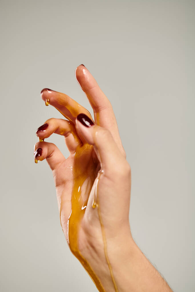 main de femme inconnue pointant vers le haut tandis que couvert de miel doux doré sur fond gris - Photo, image