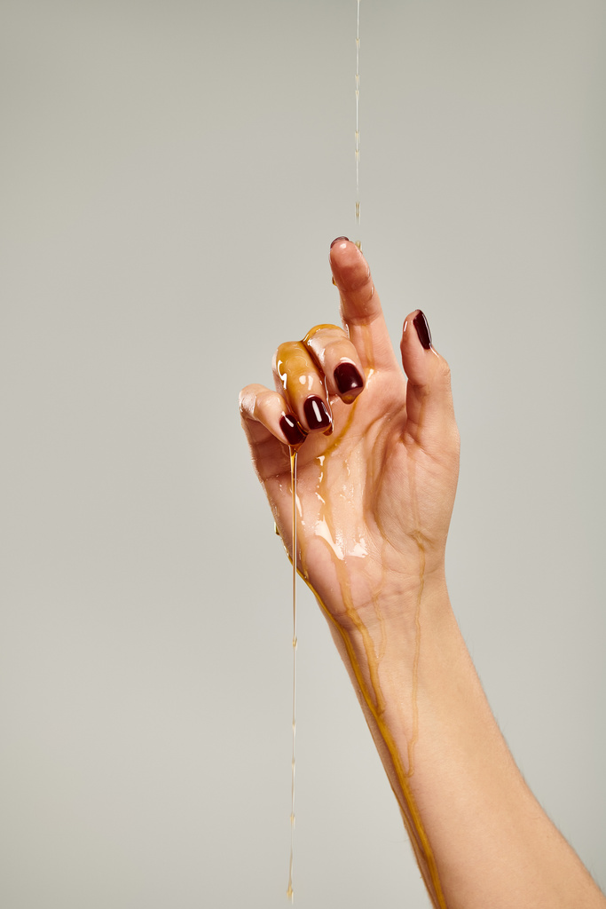χέρι άγνωστης νεαρής γυναίκας μοντέλο καλυμμένο με φυσικό νόστιμο μέλι σε γκρι φόντο - Φωτογραφία, εικόνα