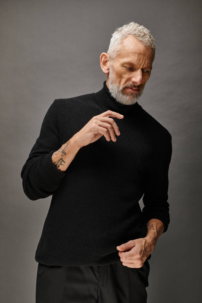 appealing fashionable mature man in trendy turtleneck posing and looking away on gray backdrop - Photo, Image