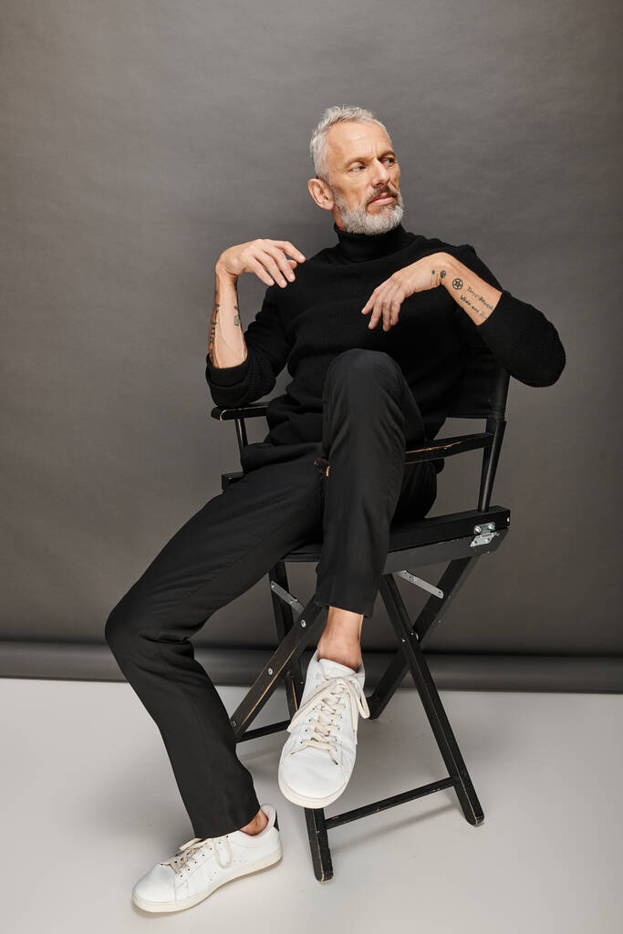 attraktives reifes männliches Modell in modischem Rollkragen auf Klappstuhl sitzend und wegschauend - Foto, Bild