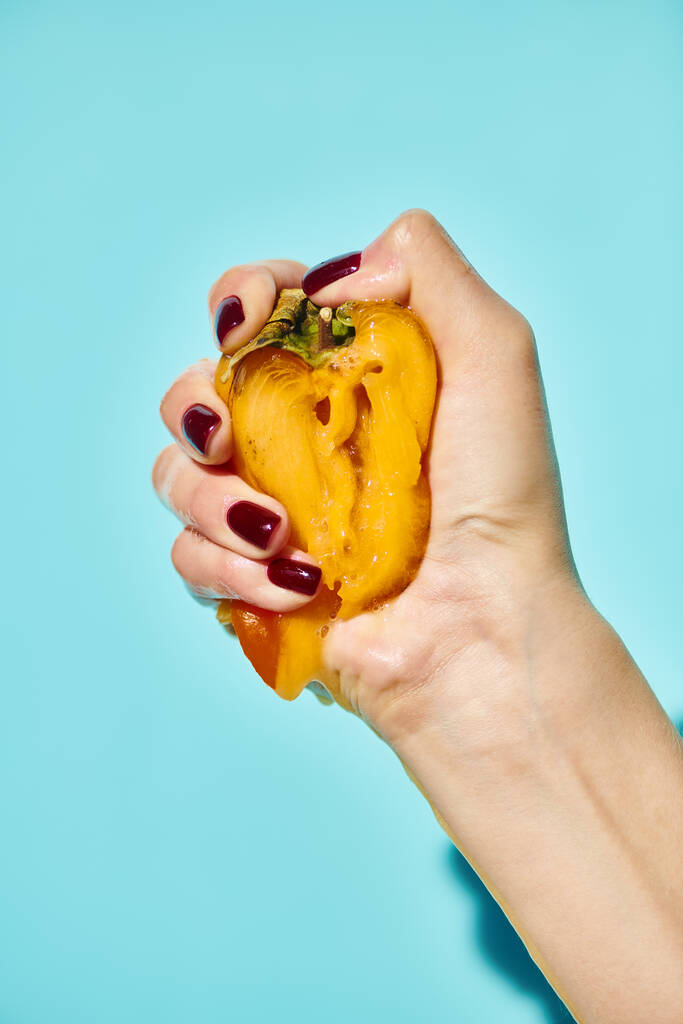 unknown woman holding tight and squeezing delicious fresh persimmon on vibrant blue background - Photo, Image