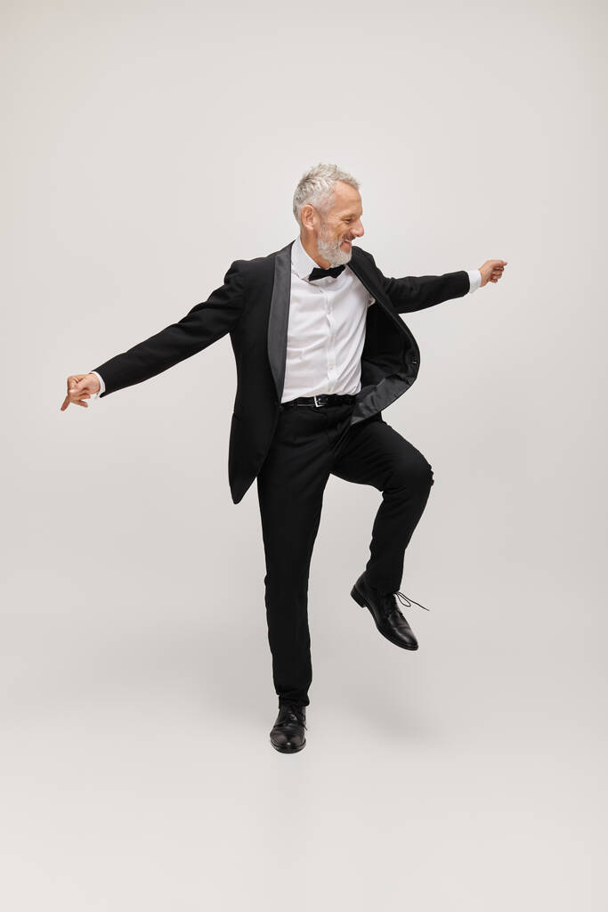 attrayant homme joyeux mature avec style élégant dapper avec barbe dansant joyeusement sur fond gris - Photo, image