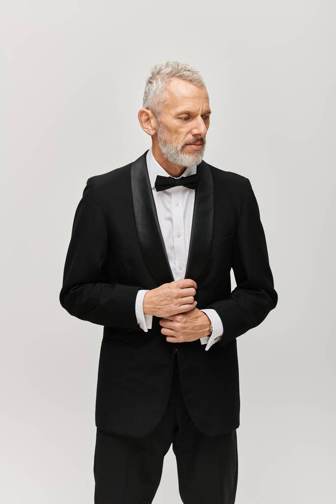 gut aussehender bärtiger älterer Mann im eleganten schwarzen Smoking mit Fliege posiert und wegschaut - Foto, Bild