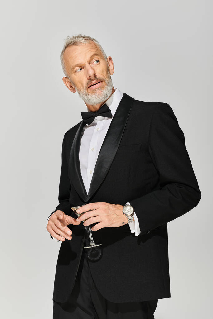 bonito barbudo maduro homem no elegante smoking com laço gravata segurando martini e olhando para longe - Foto, Imagem