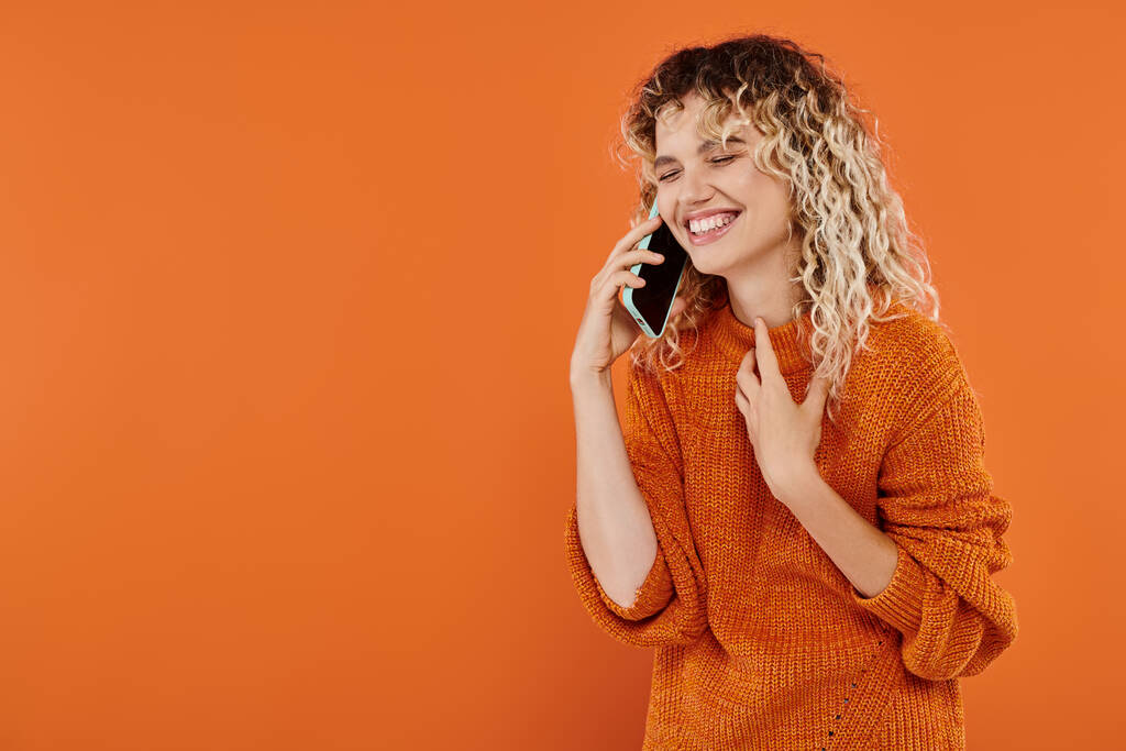 nauraa kihara nainen trendikäs neulottu villapaita puhuu matkapuhelimella kirkkaan oranssi tausta - Valokuva, kuva