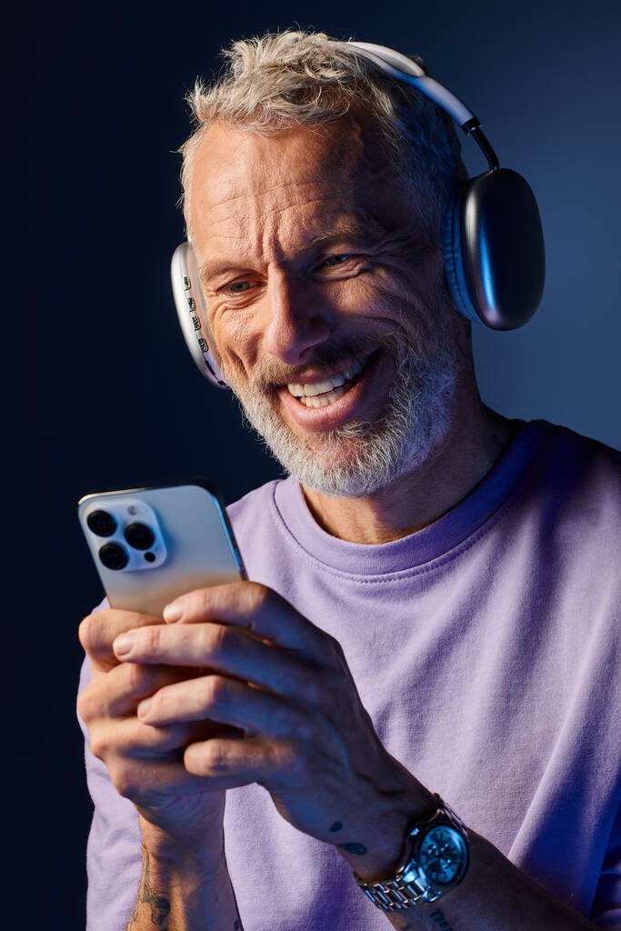 alegre bonito maduro homem com barba e fones de ouvido desfrutando de música e olhando para o seu telefone - Foto, Imagem