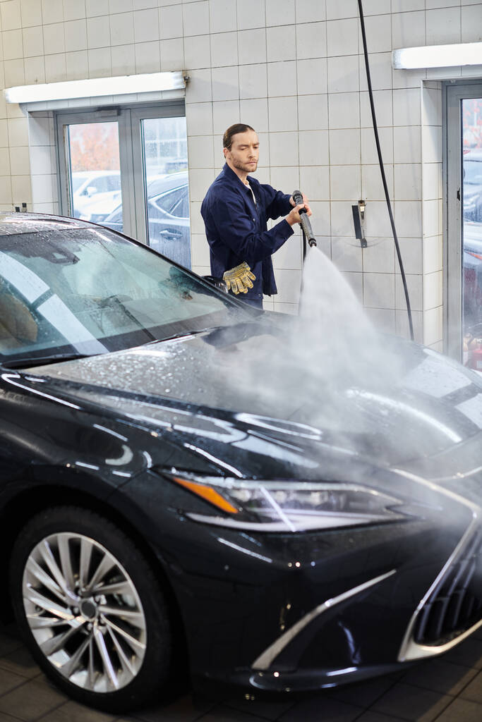 atrakcyjny pracowity profesjonalista w mundurze z zebranymi włosami myjący nowoczesny czarny samochód - Zdjęcie, obraz