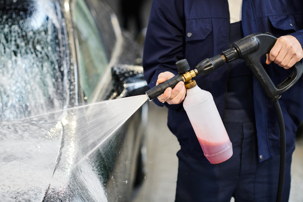 bijgesneden weergave van hard werkende professionele serviceman in blauw uniform wassen auto met zeep - Foto, afbeelding