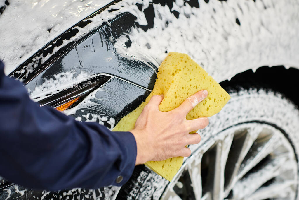 ořezaný pohled tvrdě pracující profesionál v uniformě mytí auta pomocí houby a mýdla v garáži - Fotografie, Obrázek