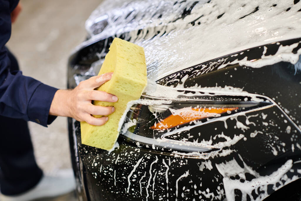 スポンジと石鹸で黒い車を洗浄するユニフォームの専用のハードワーキング男性のクロップビュー - 写真・画像