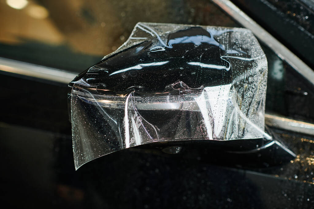 φωτογραφία αντικείμενο του καθρέφτη πλευρά του μαύρου νέου auto με μερικώς εφαρμοσμένο προστατευτικό φύλλο σε αυτό - Φωτογραφία, εικόνα
