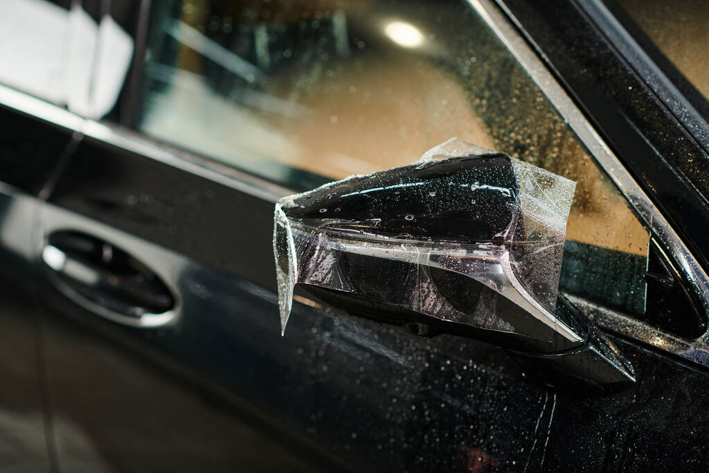 об'єктна фотографія захисної плівки, нанесеної ретельно на дзеркало чорного сучасного автомобіля - Фото, зображення