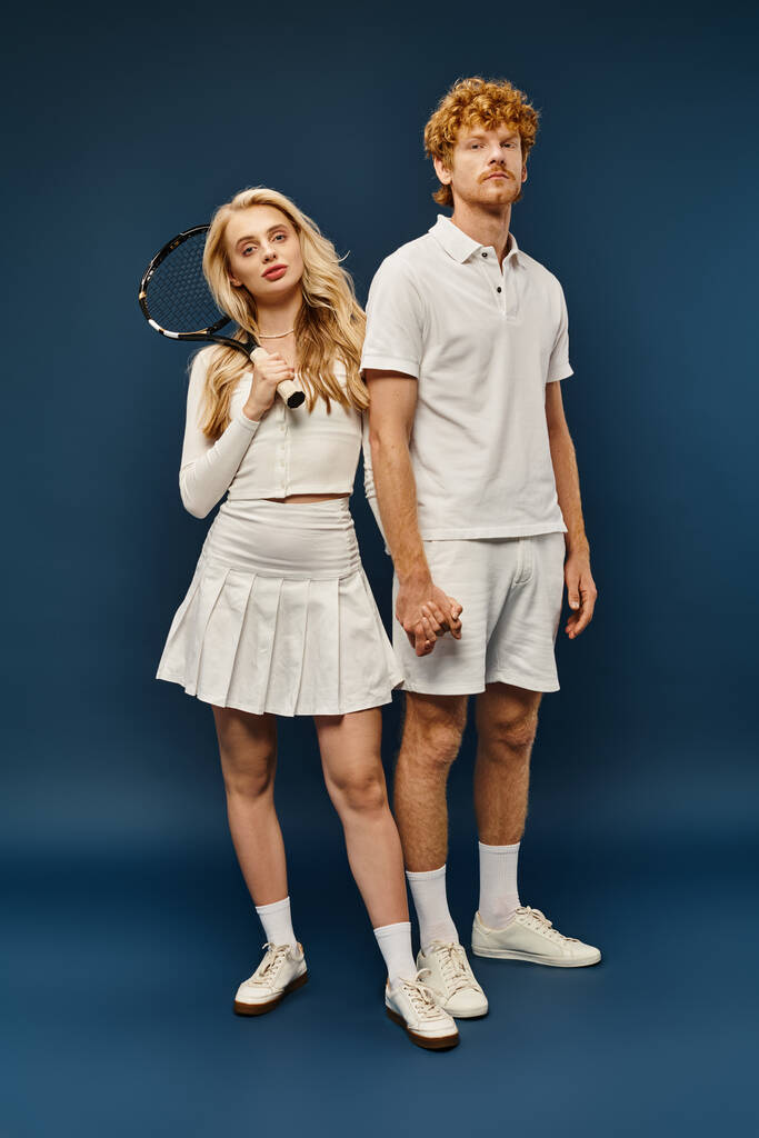 full length of blonde woman with tennis racquet near trendy redhead man in white clothes on blue - Photo, Image