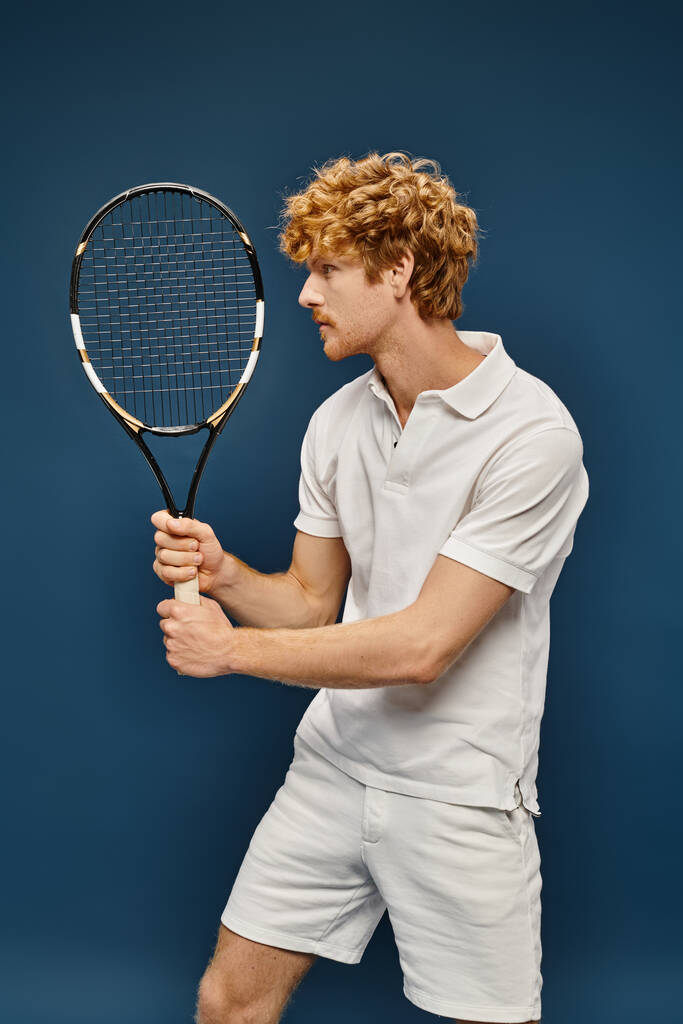 aktywny arystokratyczny rudowłosy mężczyzna w białym modnym ubraniu gra w tenisa na niebiesko, klasyczna moda - Zdjęcie, obraz