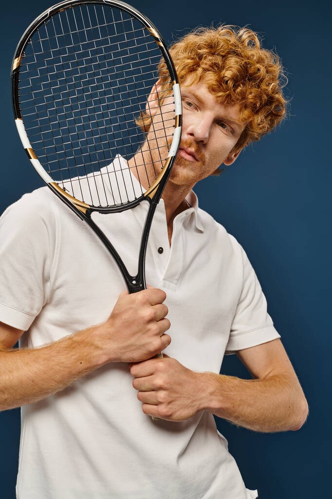 Beyaz tenisçi kıyafetli yakışıklı kızıl adam mavi yüzlü, zamansız modaya yakın raket tutuyor. - Fotoğraf, Görsel