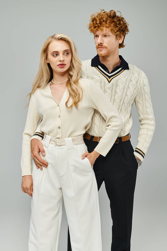 молодая аристократическая пара в модном повседневном наряде с руками в карманах на сером фоне, мода - Фото, изображение