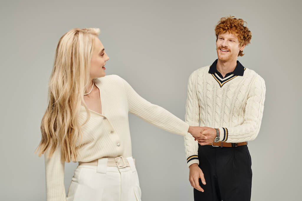 cheerful blonde woman and stylish redhead man holding hand on grey, old money style concept - Photo, Image