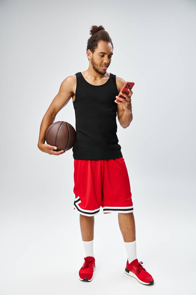 wesoły atletyczny Afroamerykanin patrzy na telefon trzymając koszykówkę, zakłady online - Zdjęcie, obraz