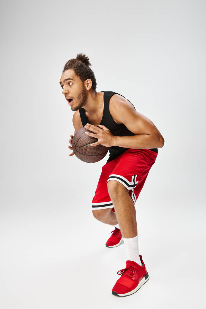mladý atletický africký Američan muž ve sportovním oblečení hrát basketbal aktivně na šedém pozadí - Fotografie, Obrázek