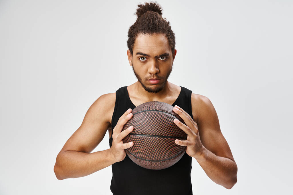 ελκυστικός αθλητικός Αφροαμερικάνος στο αθλητικό ντύσιμο κρατώντας το μπάσκετ και κοιτάζοντας την κάμερα - Φωτογραφία, εικόνα