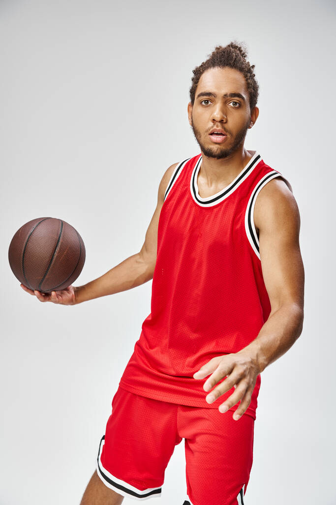 attraktive athletische afrikanisch-amerikanische Mann in lebendiger Sportbekleidung hält Basketball und blickt in die Kamera - Foto, Bild