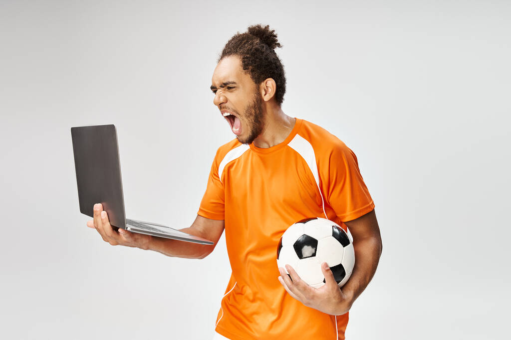 Emocjonalny Afrykanin w sportowym ubraniu trzymający piłkę nożną i oglądający laptopa, zakłady online - Zdjęcie, obraz