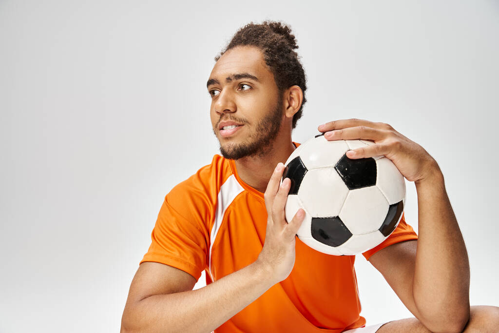 guapo alegre afroamericano deportista posando con el fútbol cerca de la cara y mirando hacia otro lado - Foto, Imagen