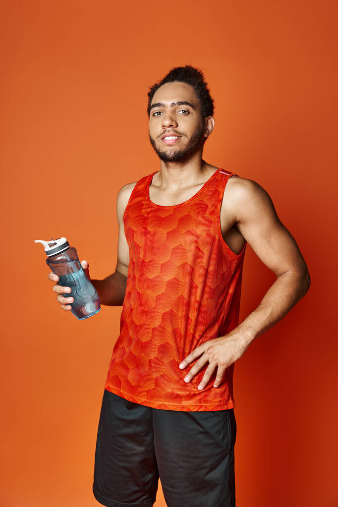 atractivo jolly afroamericano hombre en ropa deportiva celebración botella de agua y mirando a la cámara - Foto, imagen
