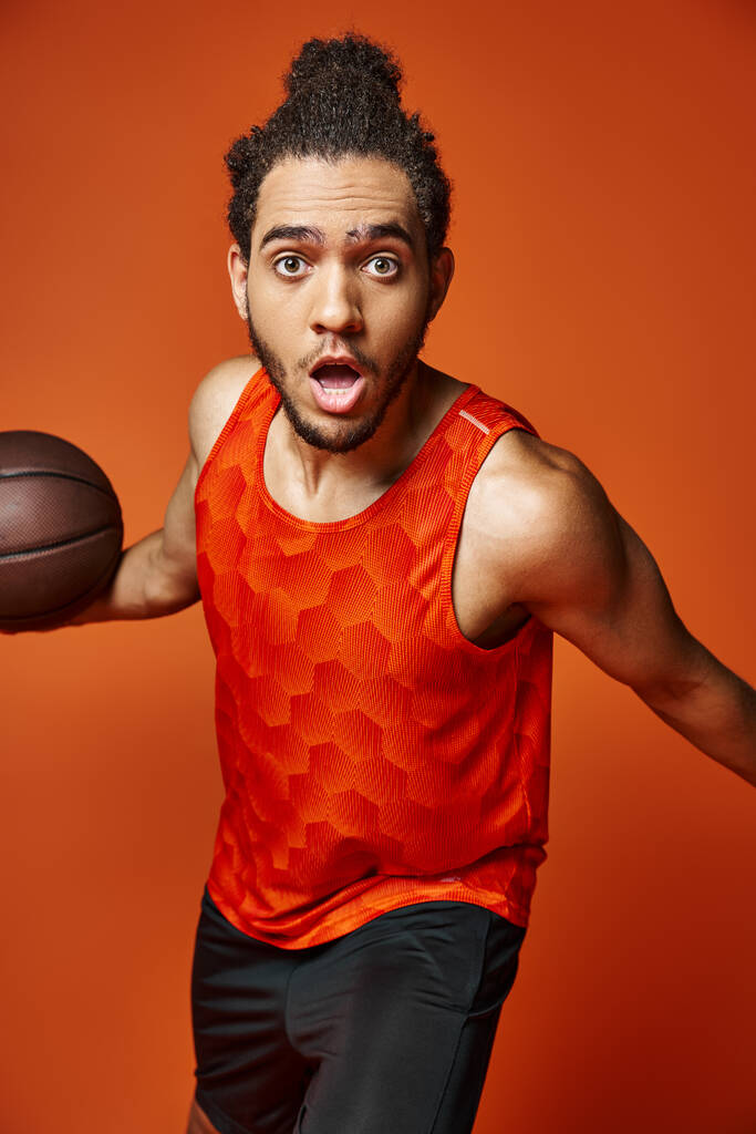 wstrząśnięty przystojny Afroamerykanin mężczyzna w sportowym ubraniu gra w koszykówkę i patrząc w aparat - Zdjęcie, obraz