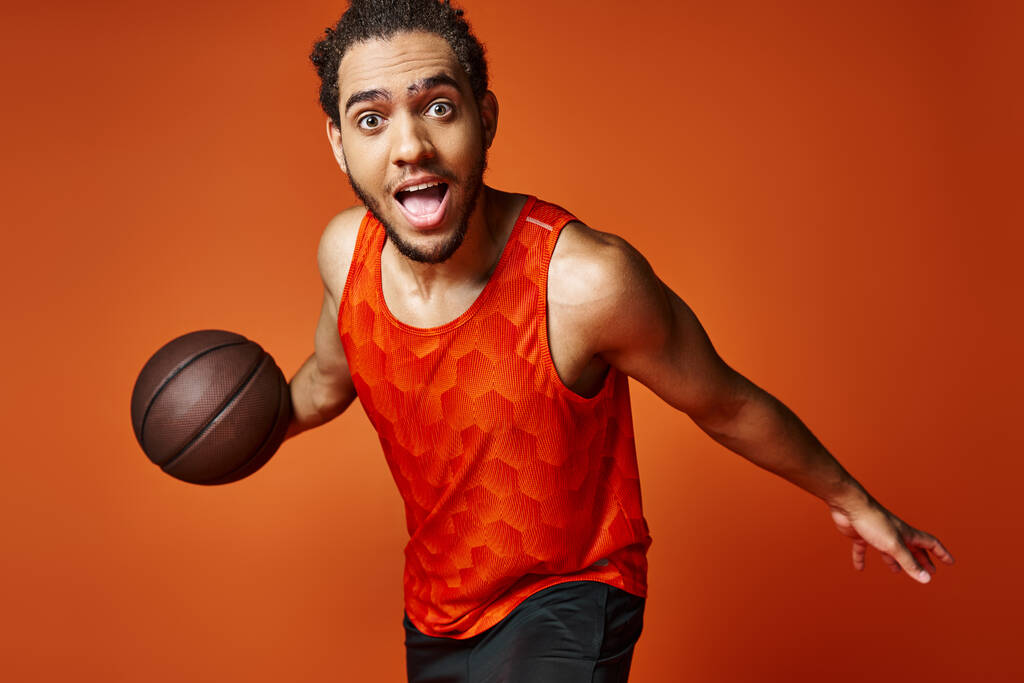 アフリカ系アメリカ人のスポーツマンが積極的にバスケットボールをし,カメラを見ていると陽気な驚き - 写真・画像