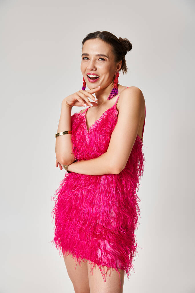 Νεαρή φωτεινή κυρία με κομψό ροζ φόρεμα που ποζάρουν ευτυχισμένοι αναζητούν στην κάμερα σε γκρι φόντο - Φωτογραφία, εικόνα