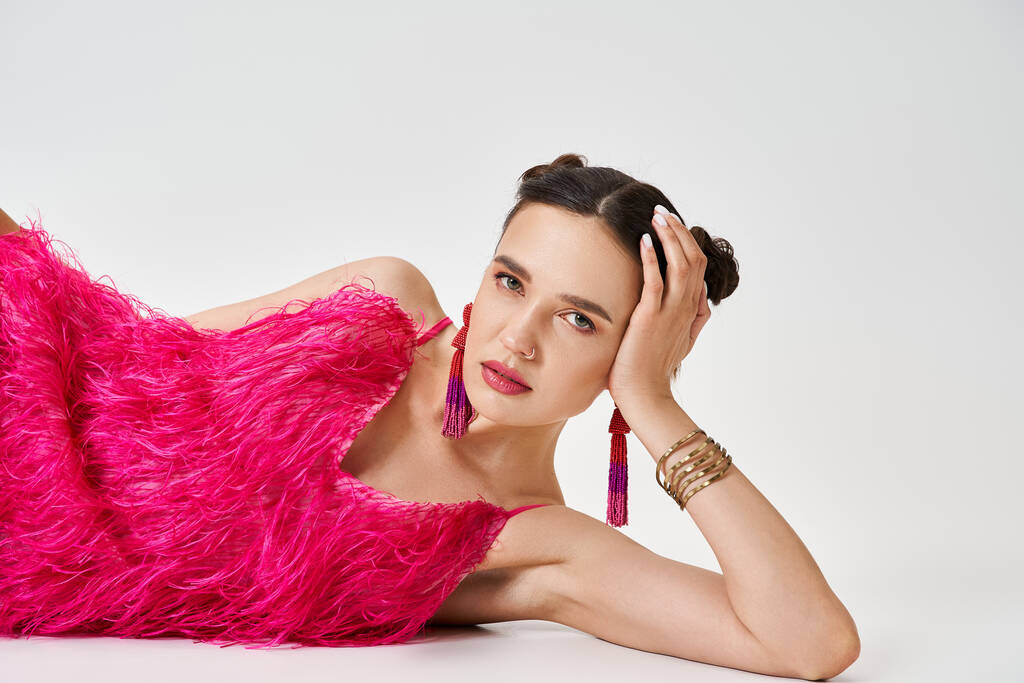 Студийный портрет уверенной брюнетки в розовом платье, лежащей головой на сером фоне - Фото, изображение