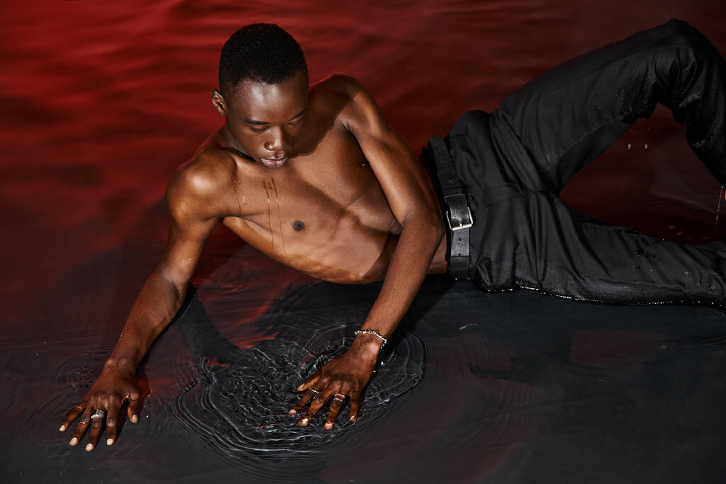 hyvännäköinen seksikäs afrikkalainen amerikkalainen mies märkä housut makuuasennossa veden pinnalla punaisissa valoissa - Valokuva, kuva