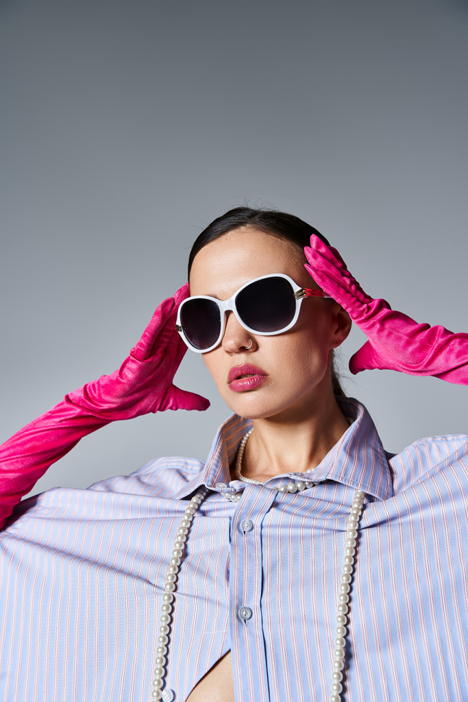Morena de moda con guantes rosas y gafas de sol de moda sobre fondo gris - Foto, Imagen