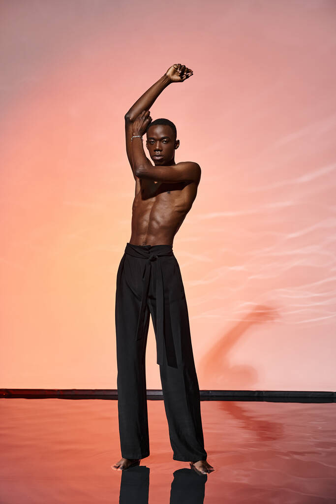 attraente uomo afroamericano senza maglietta in piedi e guardando la fotocamera circondata da luci rosse - Foto, immagini